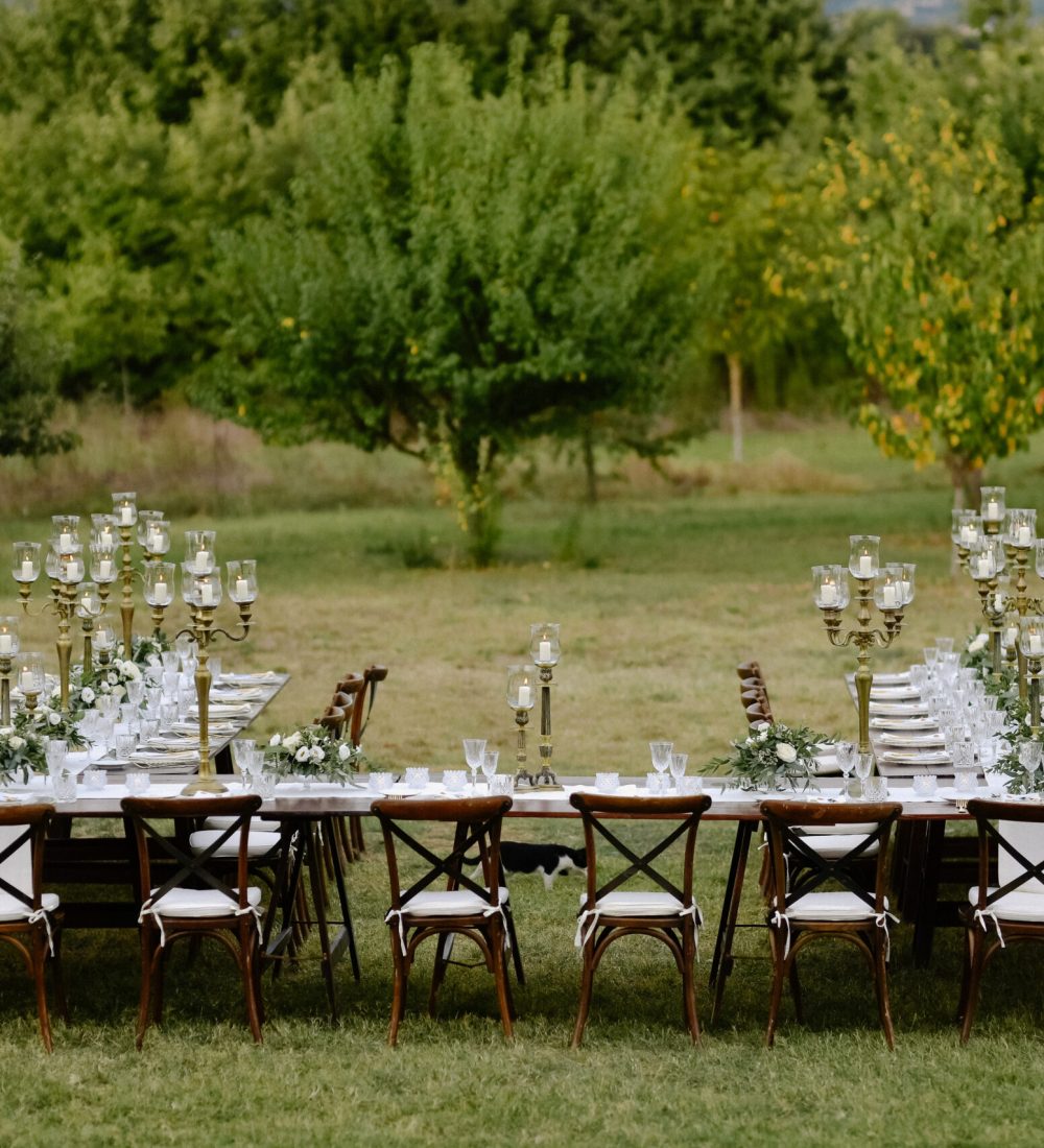 Top view of decorated with minimal floral bouquets and candles wedding celebration table with chiavari seats outdoors in the gardens in front of fruits trees